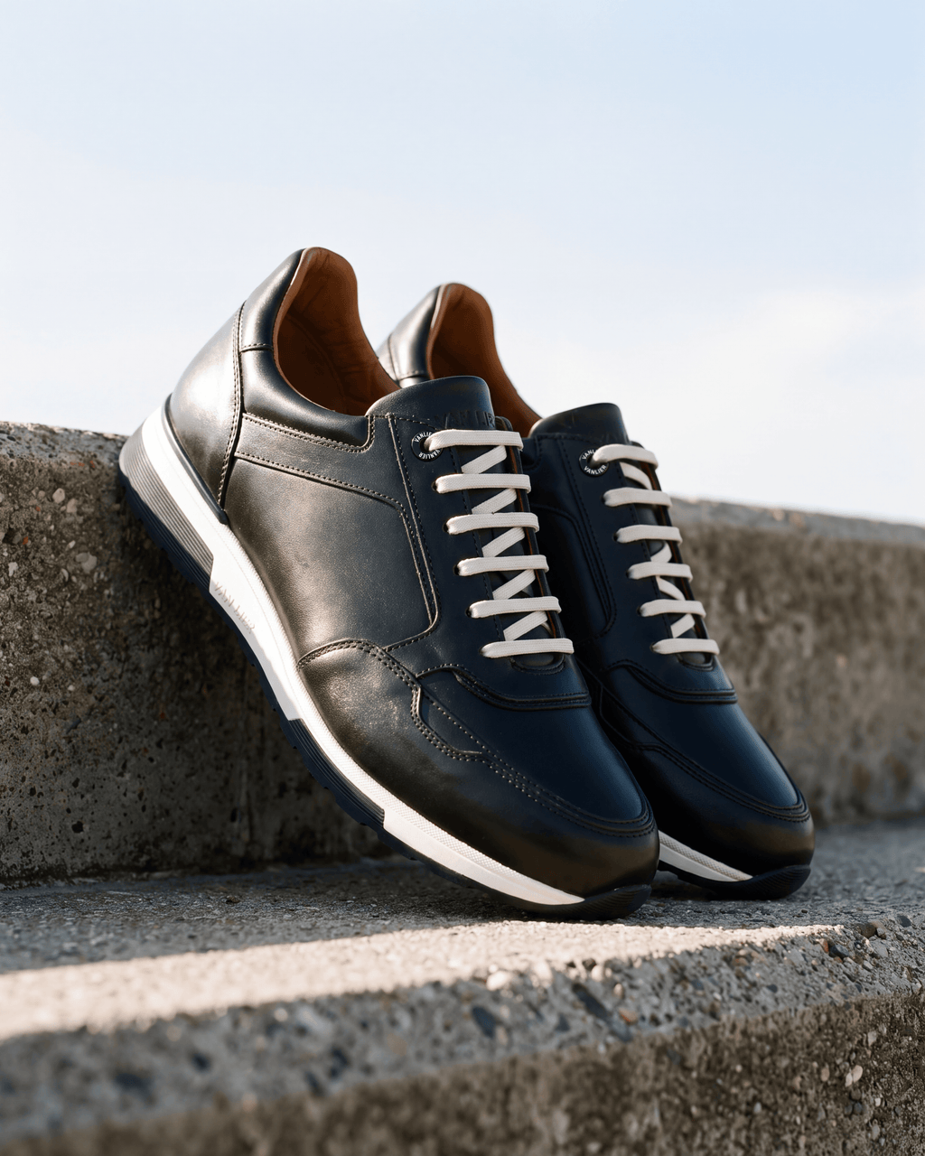 Zwart gladleren Positano sneaker – close-up van het paar op een stenen muur