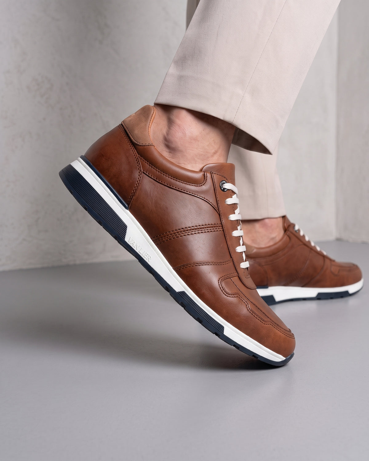 Cognac gladleren Positano sneaker – close-up van het paar in een betonnen atelier