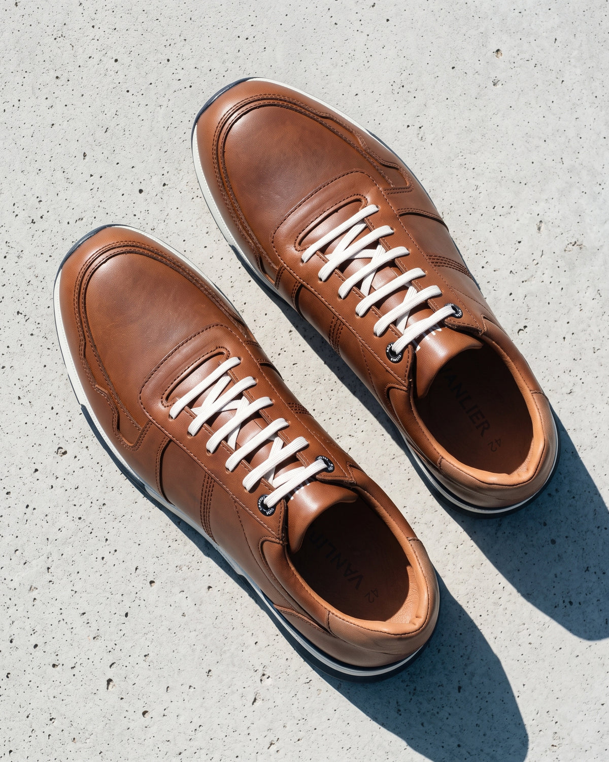 Cognac gladleren Positano sneaker – detail van het paar op ruw beton