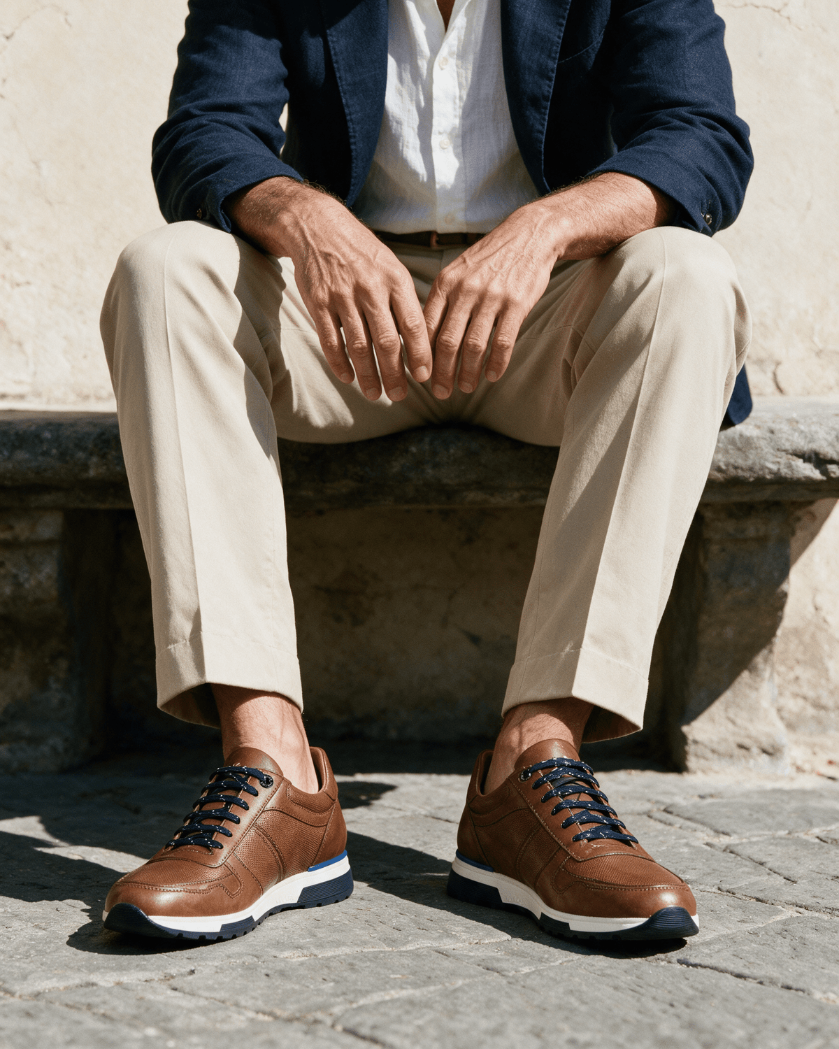Cognac gladleren Positano sneaker – gedragen, bij een stenen bank