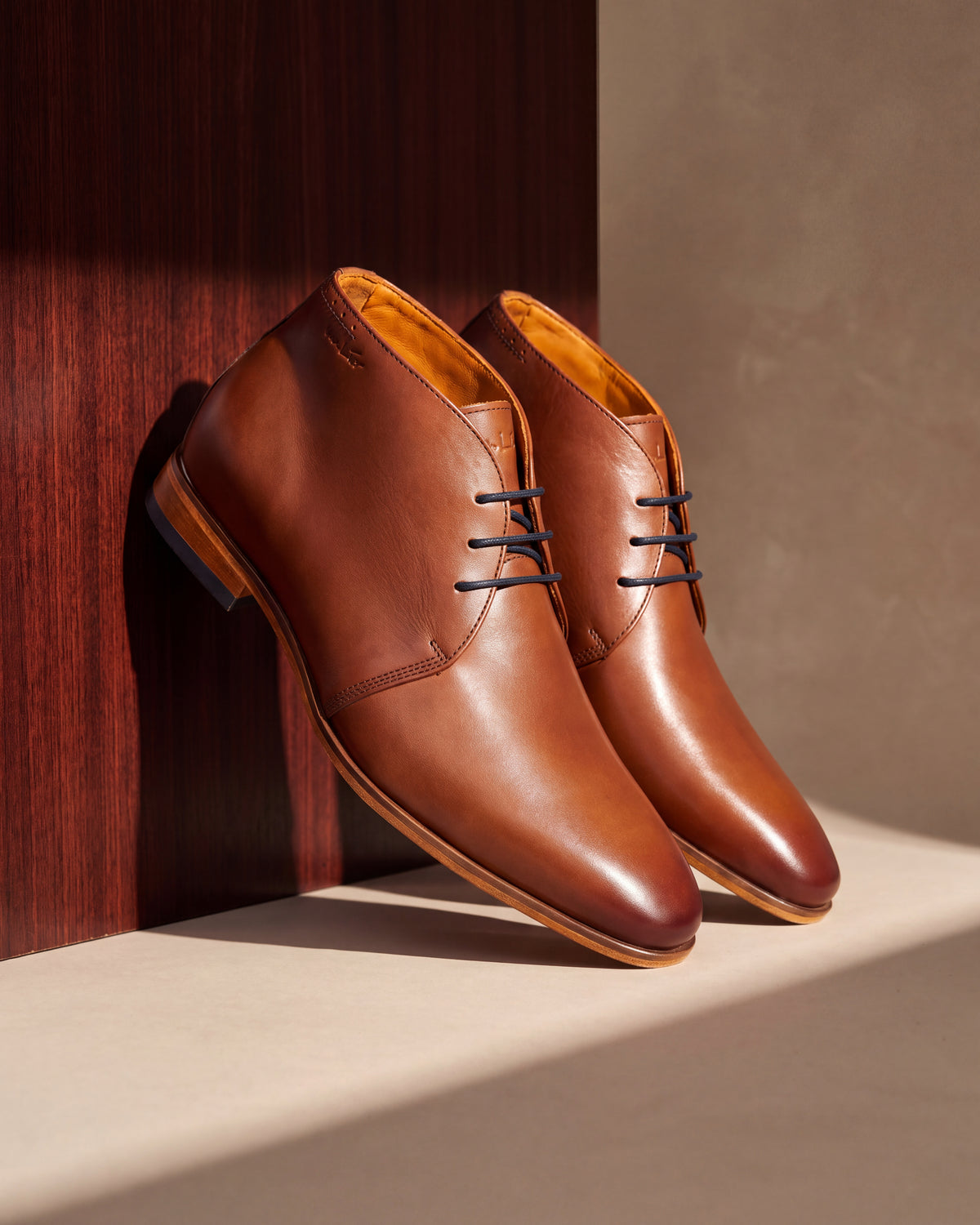 Cognac gladleren Rhodes halfhoge veterschoen – close-up van het paar tegen hout en pleisterwerk