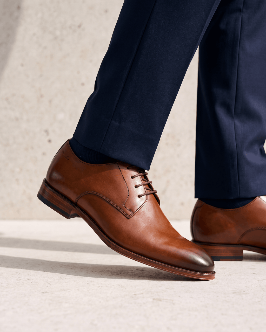 Cognac gladleren Madison veterschoen – het paar op een kalkstenen vloer