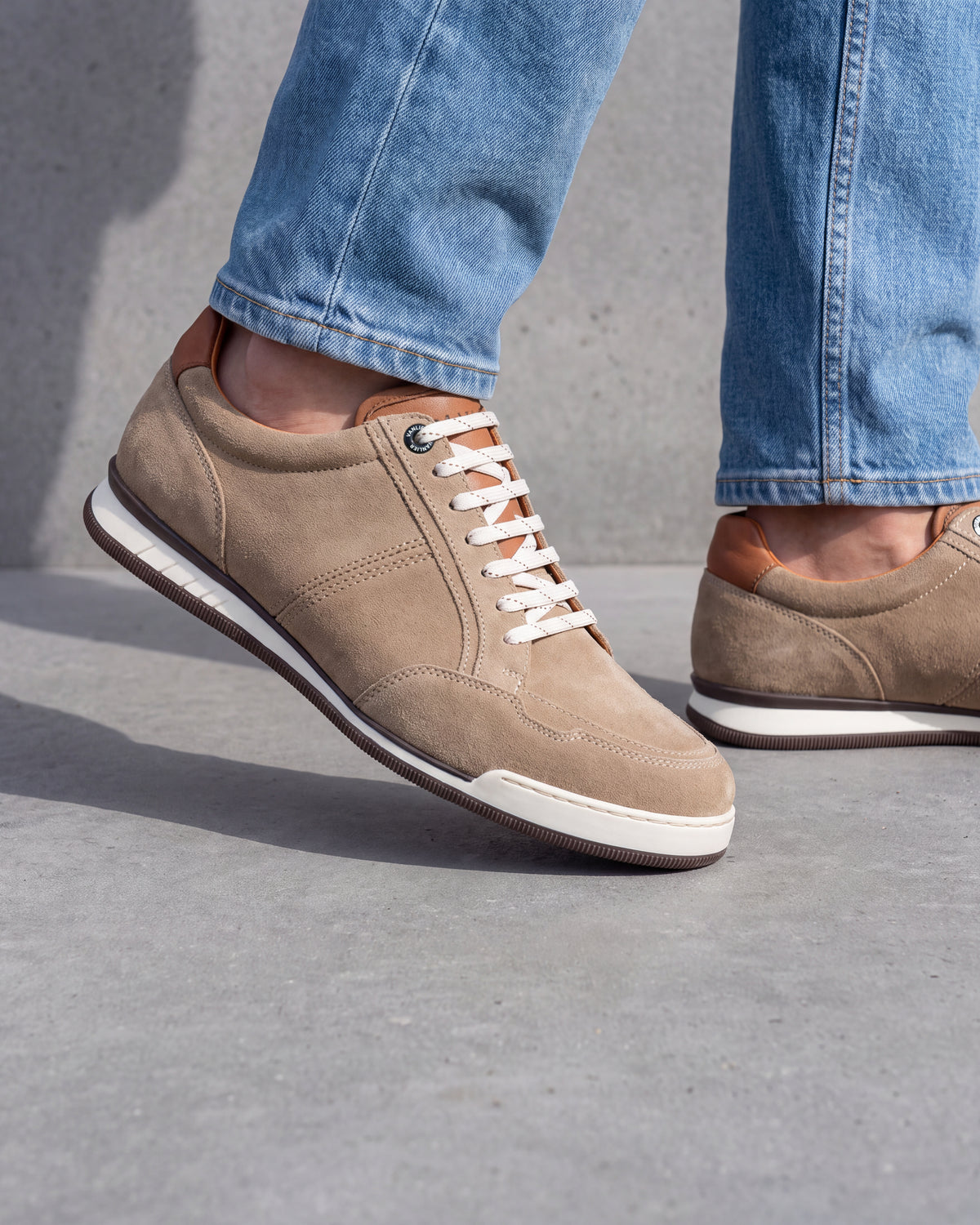 Zand beige suède Magnus sneaker – close-up van het paar op een ruwe betonnen vloer