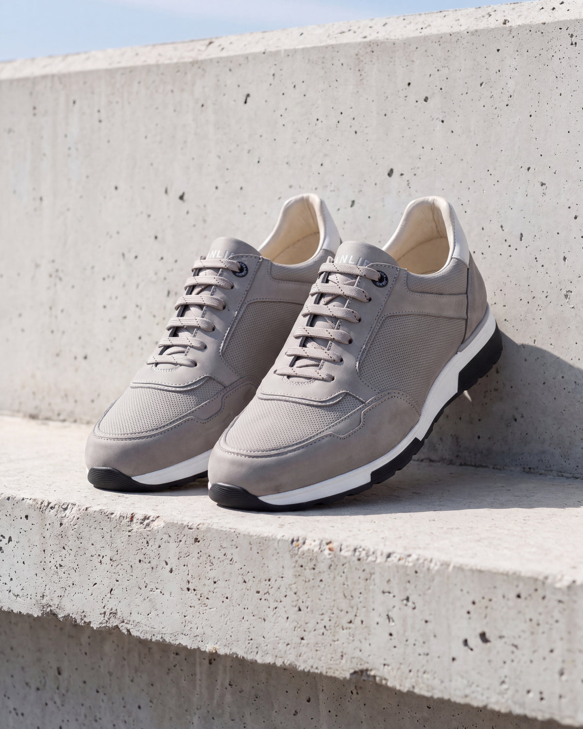 Lichtgrijs nubuck Positano sneaker – close-up van het paar op ruw beton