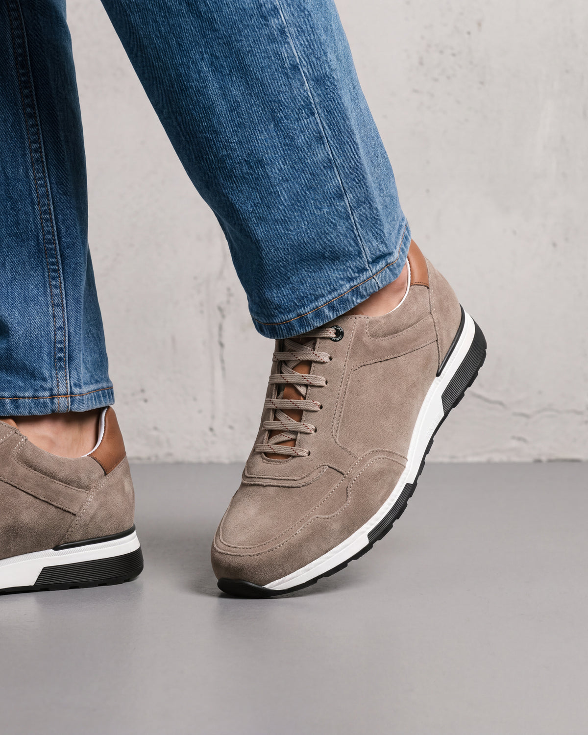 Taupe suède Positano sneaker – close-up van het paar op een betonnen vloer in een atelier