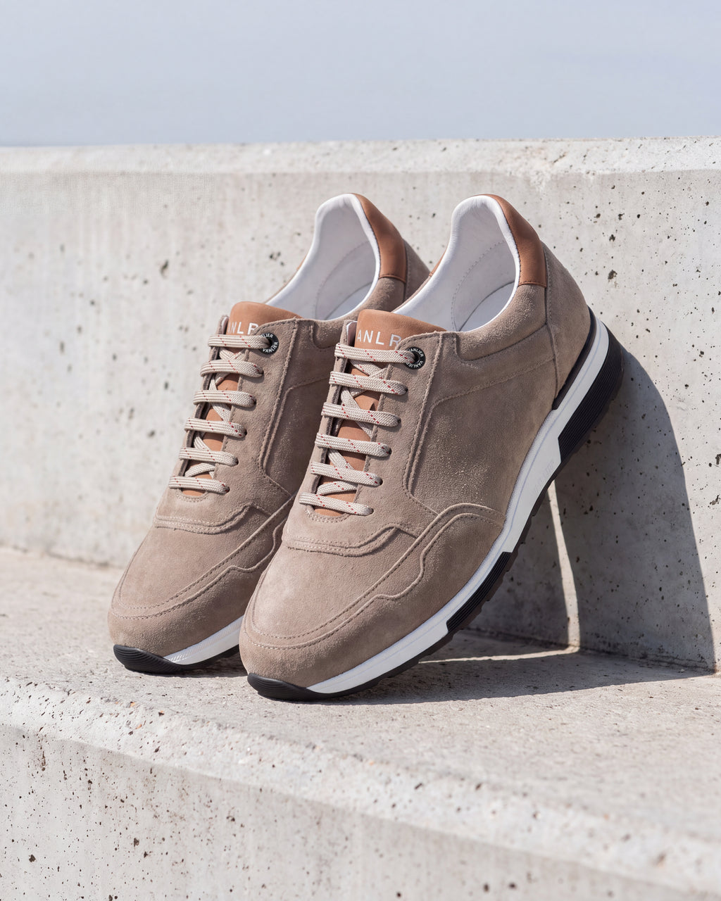 Taupe suède Positano sneaker – detail van het paar op ruw beton