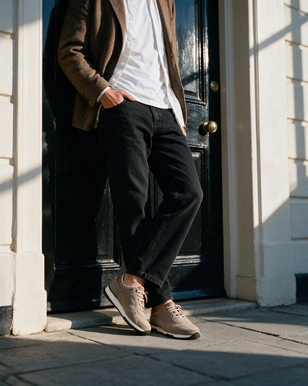 Taupe suède Positano sneaker – lifestyle tegen een zwarte deur geleund