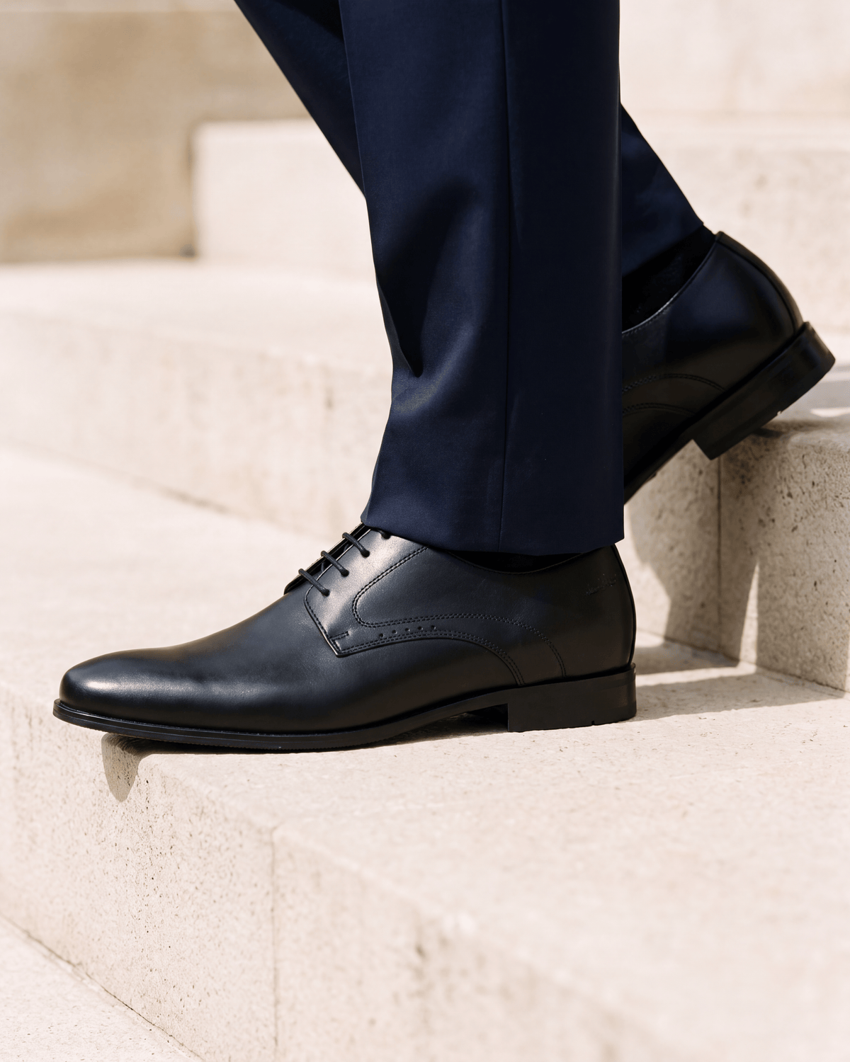 Zwart gladleren met rubberen zool Rhodes veterschoen – close-up van het paar op kalksteen